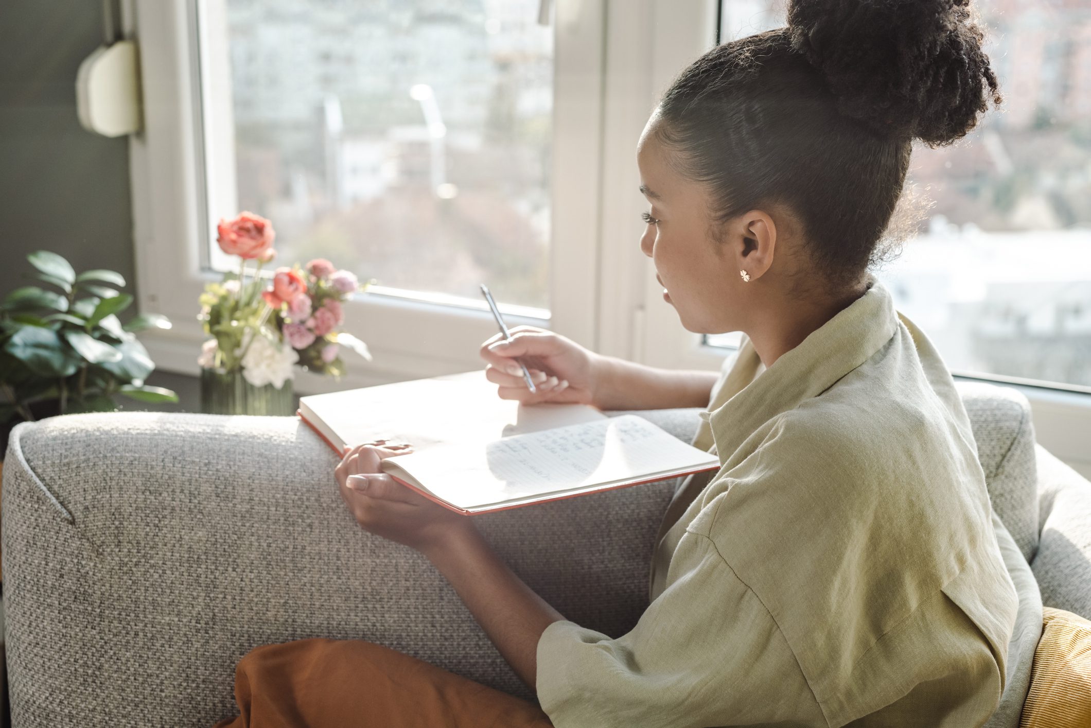 Person writing in notebook on couch by window