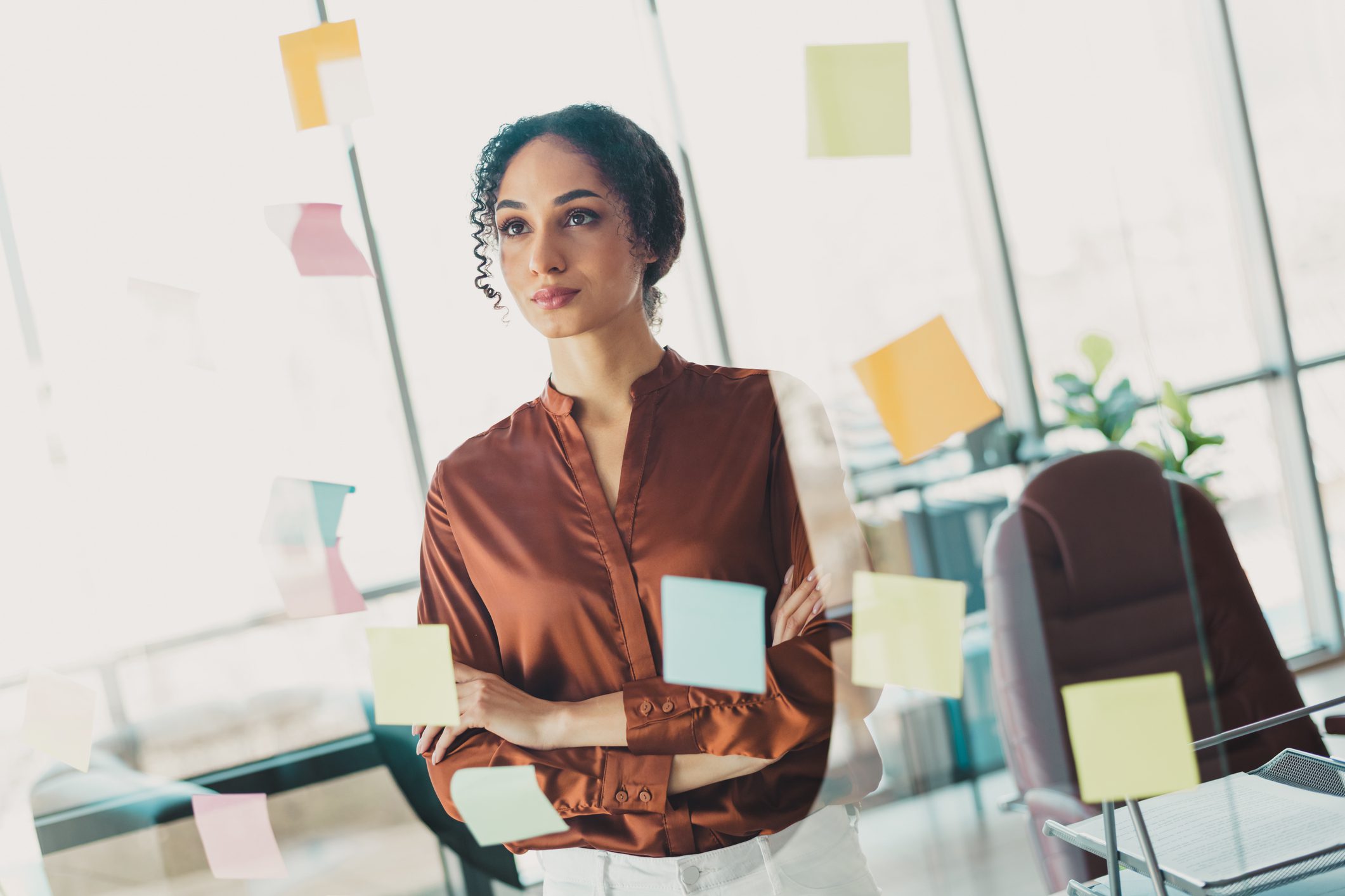 Thoughtful businesswoman standing by glass with sticky notes