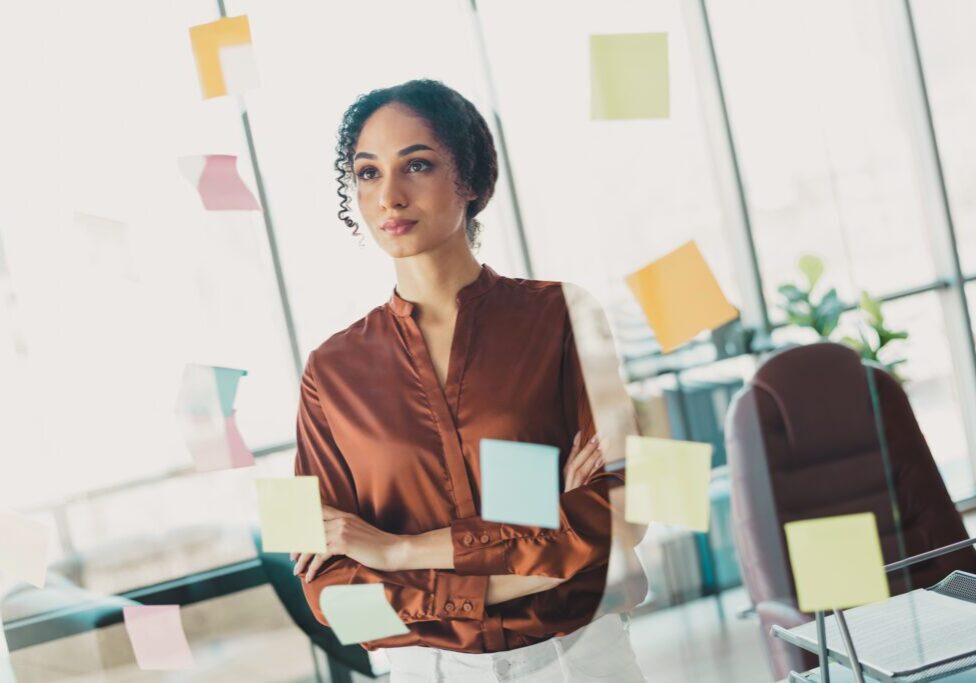Thoughtful businesswoman standing by glass with sticky notes