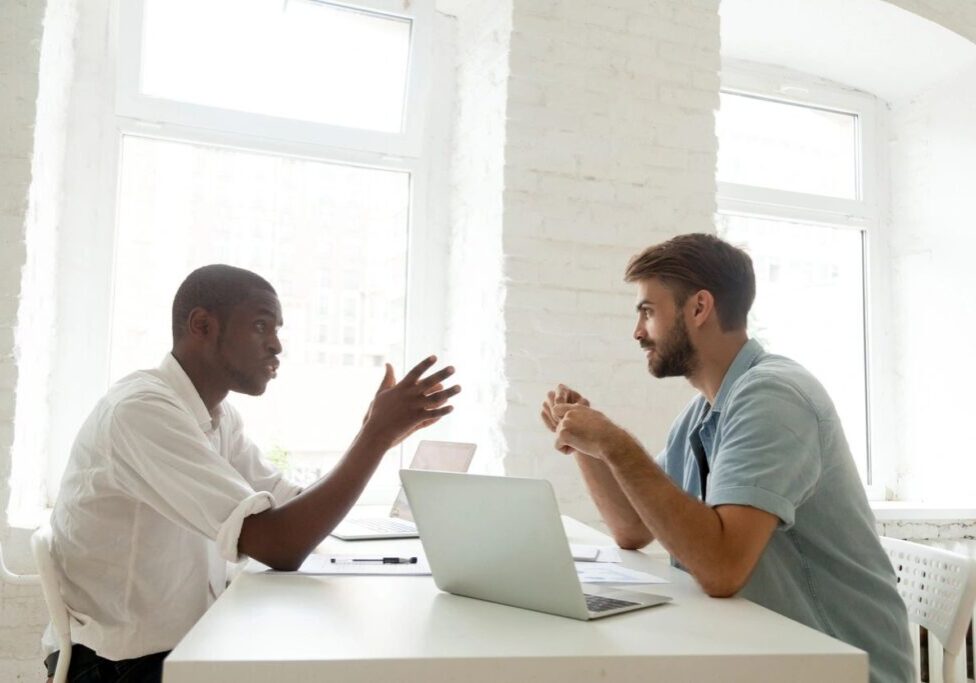 Two colleagues discussing at desk with laptop